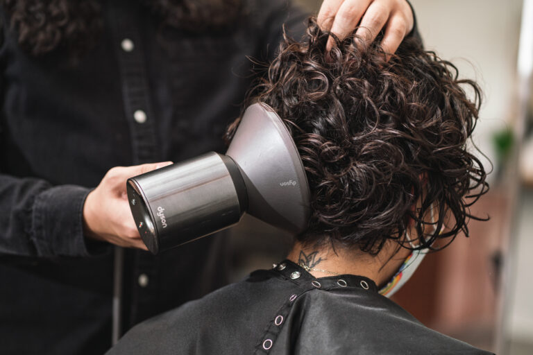 A woman with curly hair getting her hair blown dry by a stylist. This salon has experts in curly hair.